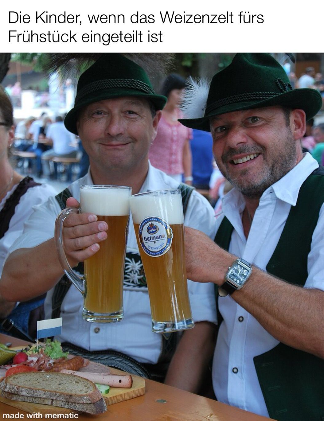 Überschrift: "Die Kinder, wenn das Weizenzelt fürs Frühstück eingeteilt ist" Bild: 2 Männer in Trachten in einem Biergarten stoßen mit Gutmann Weizen an.