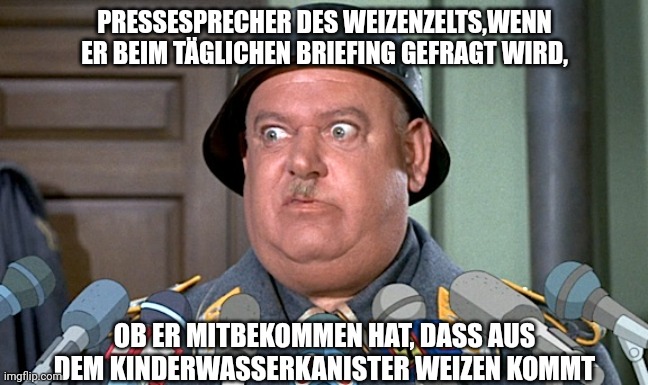 Pressesprecher des Weizenzelts, wenn er beim täglichen Briefing gefragt wird, ob er mitbekommen hat, dass aus dem Kinderwasserkanister Weizen kommt: Mann in Uniform vor mehreren Mikrofonen schaut erschrocken und panisch.